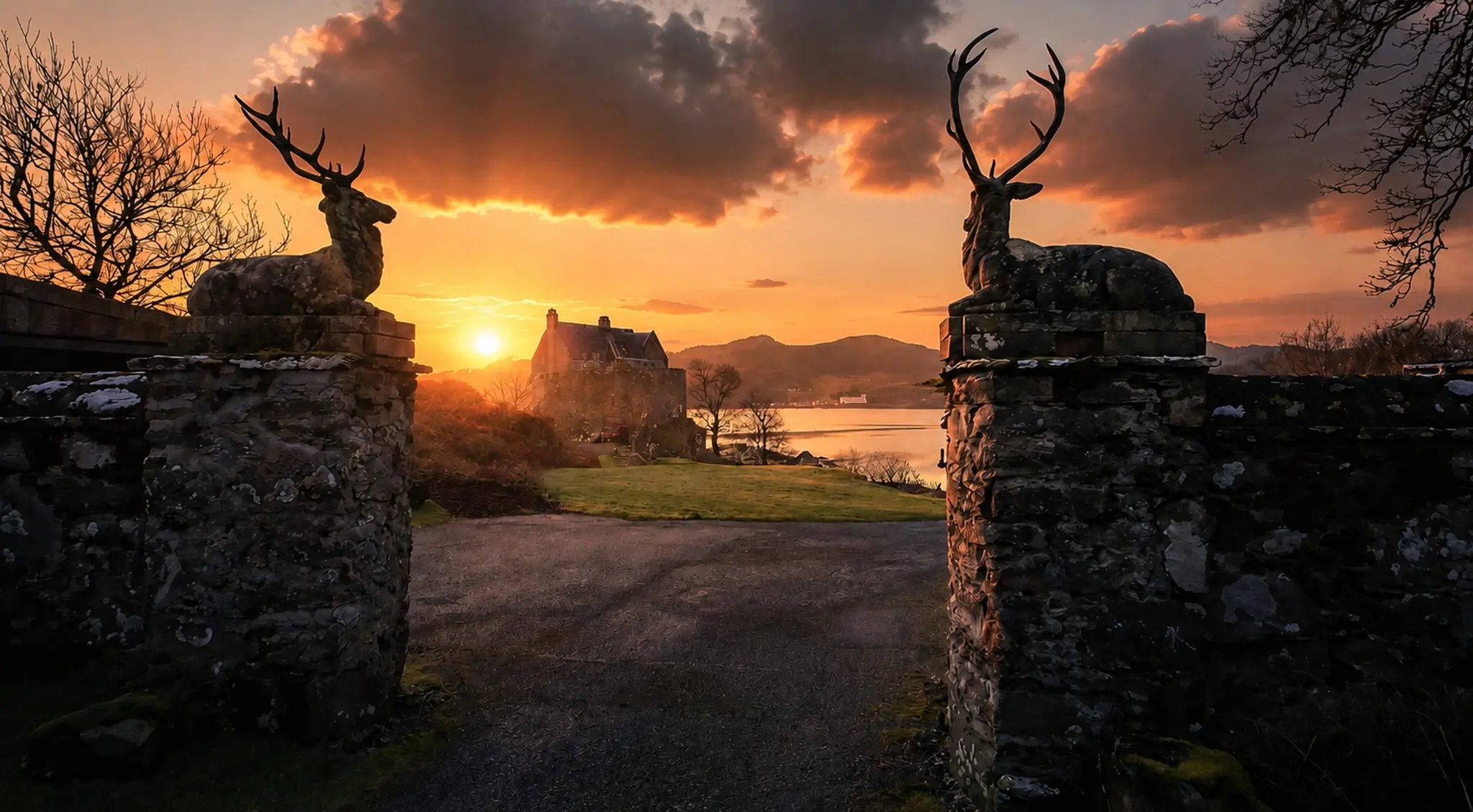 Stag sculptures framing a Highland house and loch at sunset